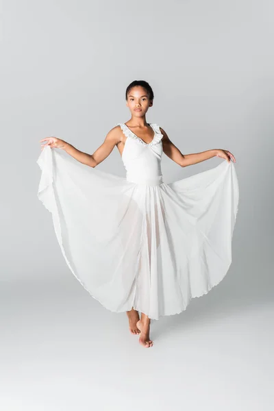 Barefoot graceful african american ballerina in dress dancing on white background — Stock Photo