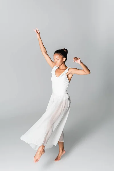 Descalza elegante bailarina afroamericana en vestido bailando sobre fondo blanco - foto de stock