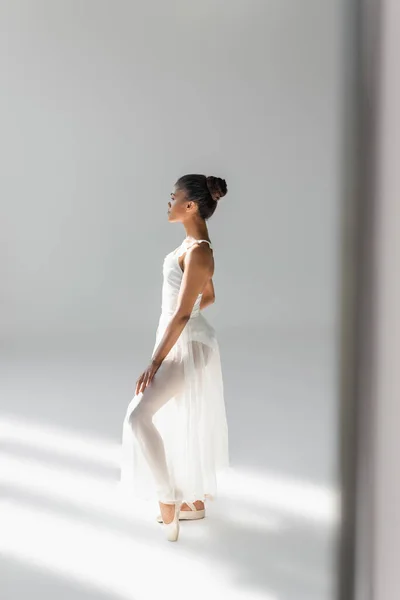 Vista lateral de la elegante bailarina afroamericana en vestido sobre fondo blanco - foto de stock