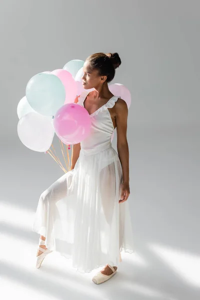 Graceful african american ballerina in dress with balloons on white background — Stock Photo