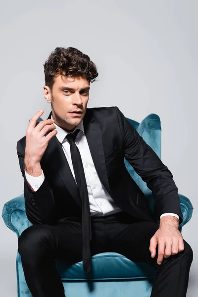 Elegant man in suit sitting in velour armchair isolated on grey — Stock Photo