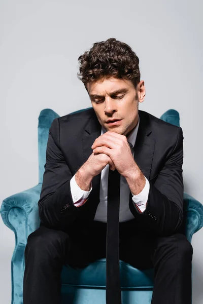 Pensive elegant man in suit sitting in velour armchair isolated on grey — Stock Photo