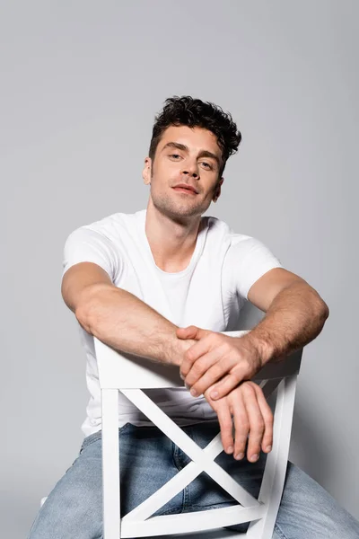 Young man in white t-shirt sitting on chair isolated on grey — Stock Photo