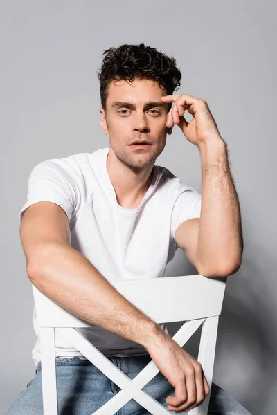 Young man in white t-shirt sitting on chair isolated on grey — Stock Photo