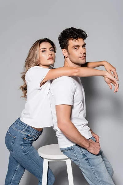 Vue latérale du jeune couple en t-shirts blancs câlins isolés sur gris — Photo de stock