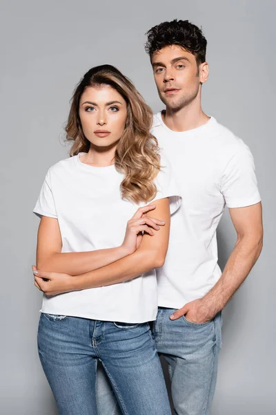 Young couple in white t-shirts and jeans posing isolated on grey — Stock Photo