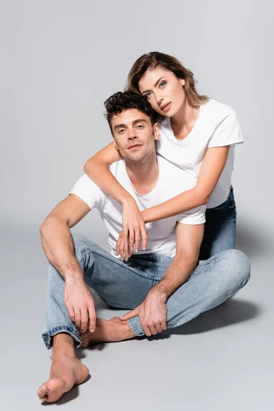 Jeune couple en t-shirts blancs embrassant isolé sur gris — Photo de stock