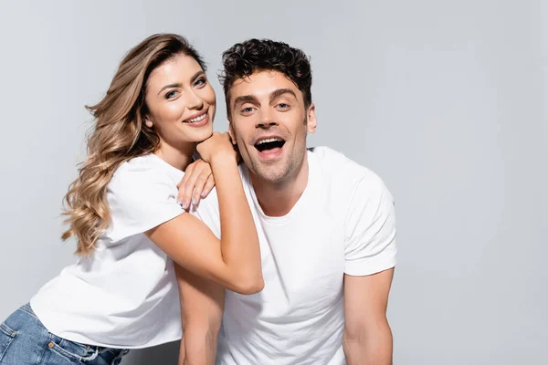 Feliz joven pareja en blanco camisetas posando aislado en gris - foto de stock