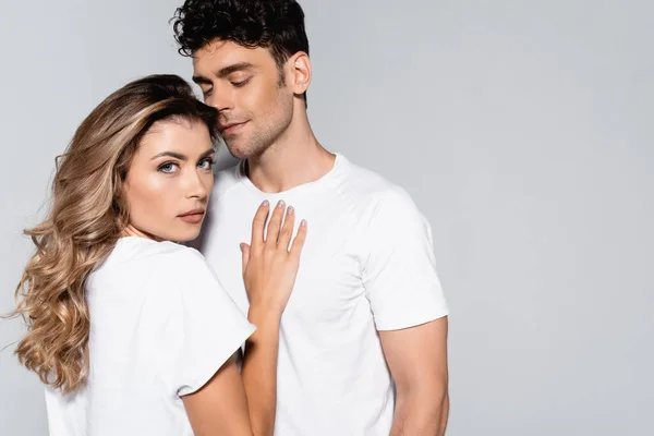 Jeune couple en t-shirts blancs posant isolé sur gris — Photo de stock