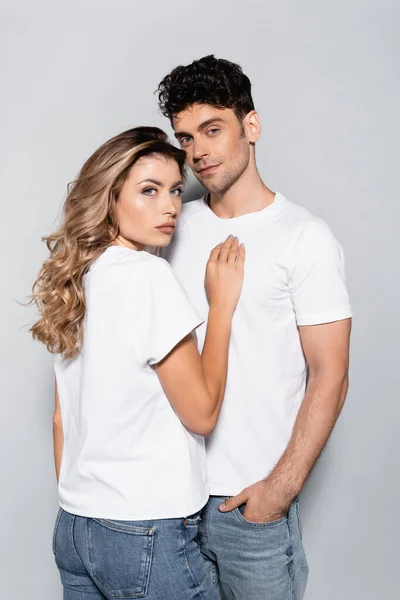 Jovem casal em camisetas brancas posando isolado no cinza — Fotografia de Stock