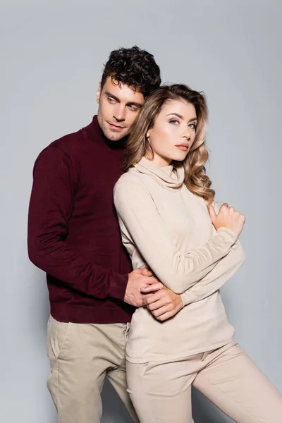 Casual young couple in turtleneck jumpers embracing isolated on grey — Stock Photo