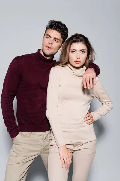 Casual giovane coppia in maglioni dolcevita che abbraccia isolato su grigio — Foto stock