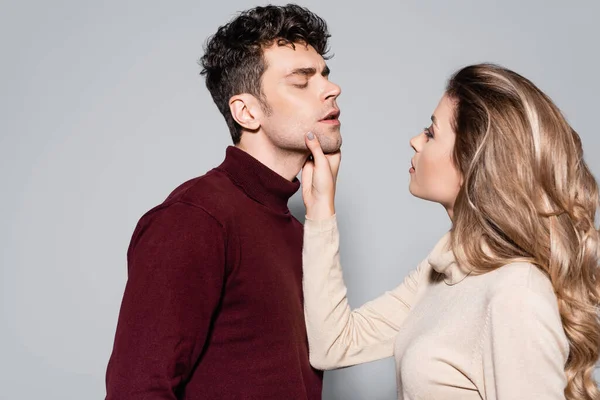 Giovane donna in maglione dolcevita che tiene il viso dell'uomo isolato sul grigio — Foto stock