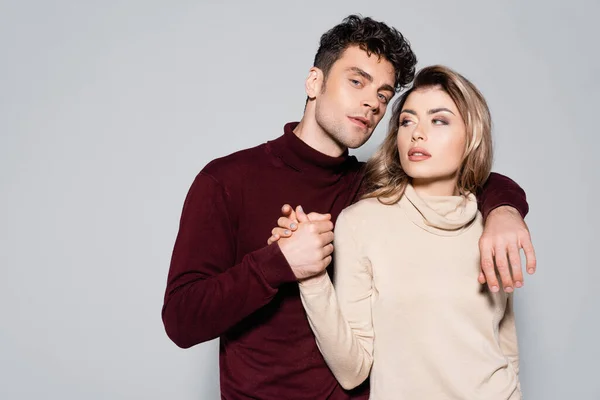 Casual jeune couple en col roulé sauteurs tenant les mains isolées sur gris — Photo de stock