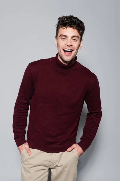 Happy young man in burgundy turtleneck jumper posing isolated on grey — Stock Photo