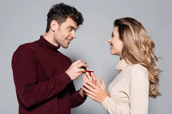 Occasionnel jeune homme faire mariage demande en mariage à heureux femme isolé sur gris — Photo de stock