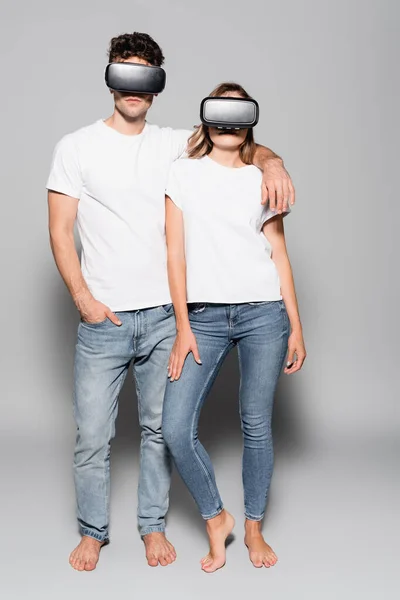 Casual pareja joven en camisetas blancas y auriculares vr aislados en gris - foto de stock
