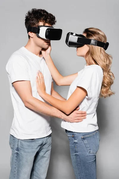 Casual young couple in white t-shirts and vr headsets isolated on grey — Stock Photo