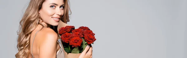 Femme élégante et souriante en robe avec bouquet de roses rouges isolé sur gris, bannière — Photo de stock