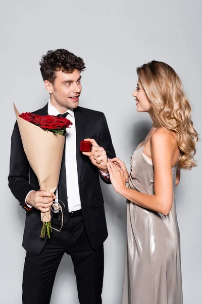 Elegante giovane uomo con bouquet facendo proposta di matrimonio isolato su grigio — Foto stock