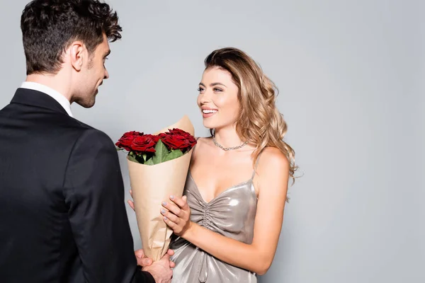 Elegante giovane uomo regalando bouquet alla donna isolata su grigio — Foto stock