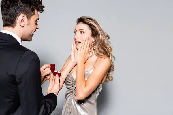 Elegante joven haciendo propuesta de matrimonio aislado en gris - foto de stock