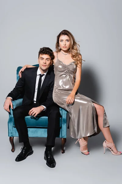 Elegant young couple posing in velour armchair isolated on grey — Stock Photo