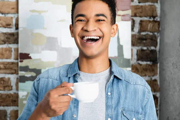 Здивований американець - афроамериканець сміється, тримаючи в руках каву. — стокове фото