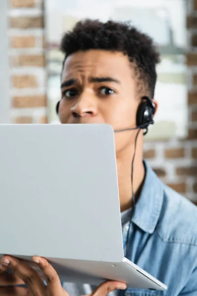 African american assistant in headset holding laptop — Stock Photo