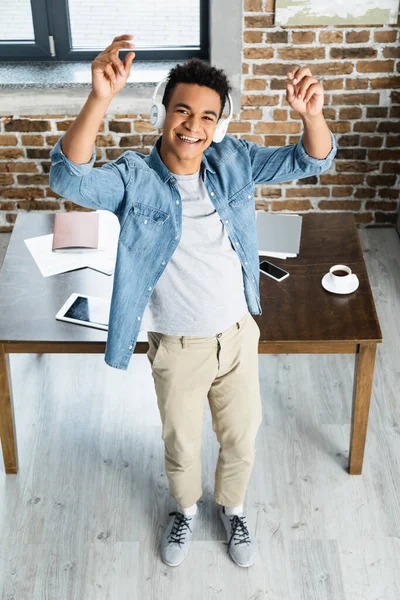 Vista ad alto angolo di felice uomo africano americano in piedi vicino alla scrivania con gadget — Foto stock