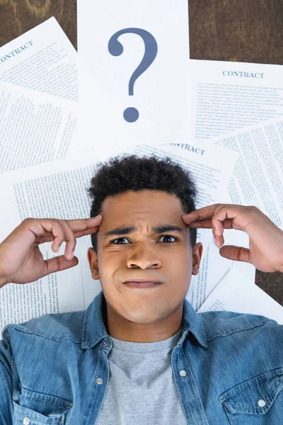 Vue de dessus de cher homme afro-américain regardant la caméra près des documents avec lettrage contractuel sur le bureau — Photo de stock