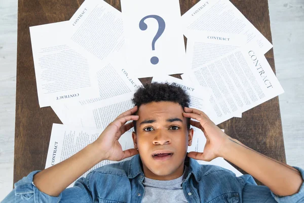 Vue de dessus de l'homme afro-américain choqué regardant la caméra près des documents avec lettrage contractuel sur le bureau — Photo de stock