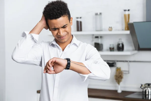 Hombre afroamericano acentuado mirando el reloj en la mano - foto de stock