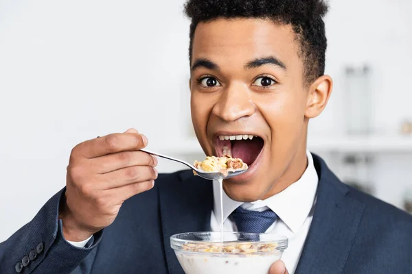 Sorprendido hombre de negocios afroamericano comiendo hojuelas de maíz con leche - foto de stock