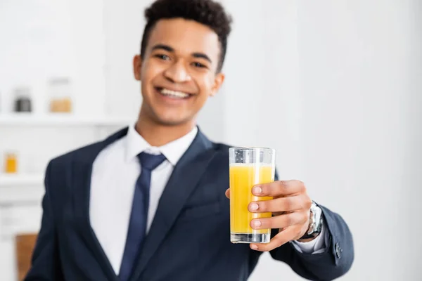 Vaso de jugo de naranja en la mano del empresario afroamericano feliz sobre fondo borroso - foto de stock