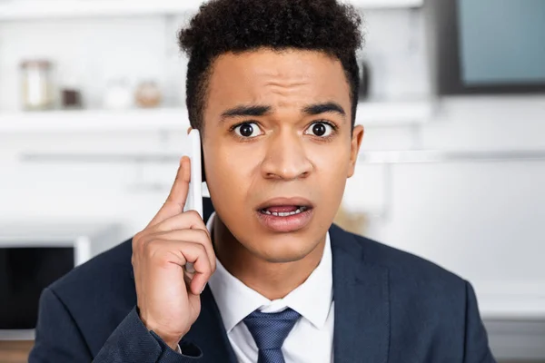 Shocked african american businessman looking at camera while talking on smartphone — Stock Photo