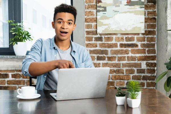 Surprised african american man looking at camera near laptop on desk — Stock Photo