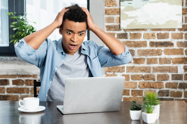 Stressato uomo africano americano guardando computer portatile vicino tazza sulla scrivania — Foto stock