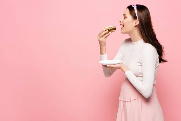 Felice giovane bella donna incinta mangiare torta isolato su rosa — Foto stock