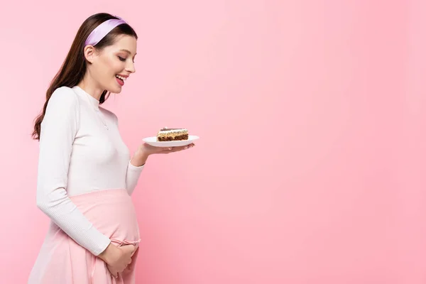 Heureux jeune jolie femme enceinte avec gâteau isolé sur rose — Photo de stock