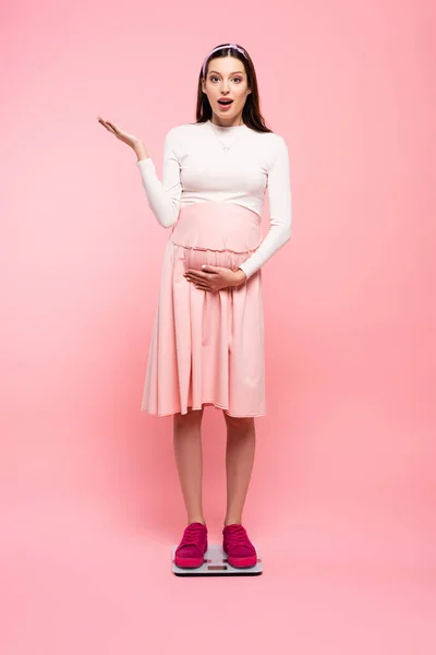 Shocked young pretty pregnant woman on scales isolated on pink — Stock Photo