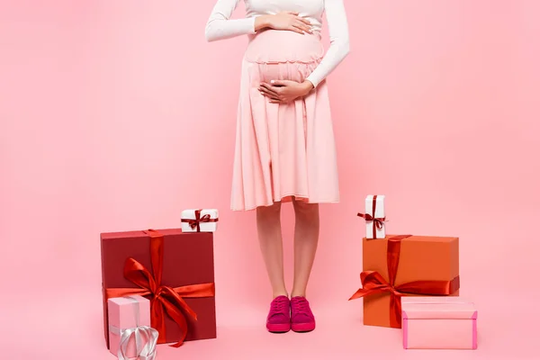 Cropped view of young pretty pregnant woman with presents isolated on pink — Stock Photo