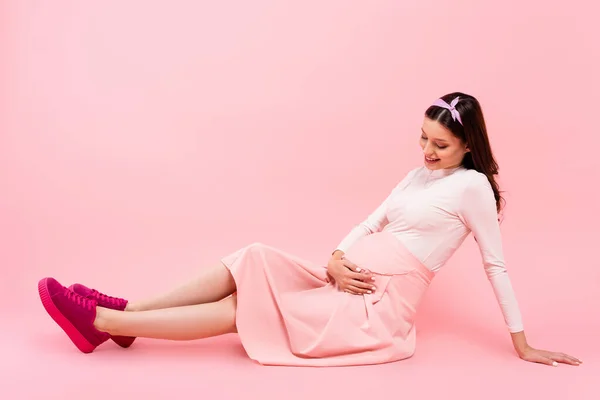 Souriant jeune jolie femme enceinte assis sur le sol isolé sur rose — Photo de stock