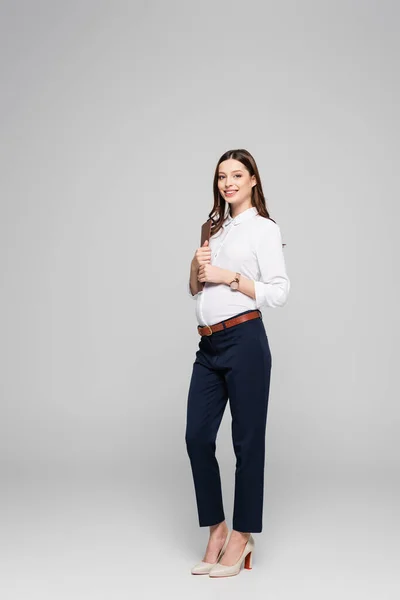 Sonriente joven embarazada mujer de negocios con carpeta aislada en gris - foto de stock