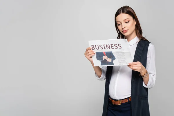 Young pregnant businesswoman holding business newspaper isolated on grey — Stock Photo