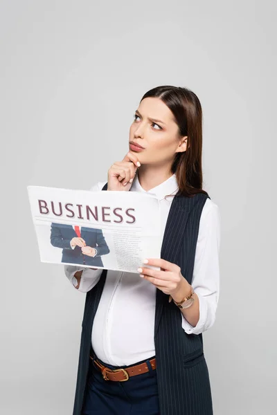 Pensive young pregnant businesswoman holding business newspaper isolated on grey — Stock Photo