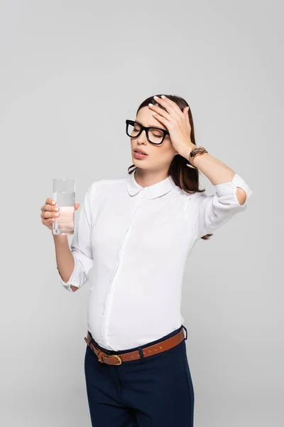 Уставшая молодая беременная деловая женщина в стаканах со стаканом воды, изолированной на сером — стоковое фото