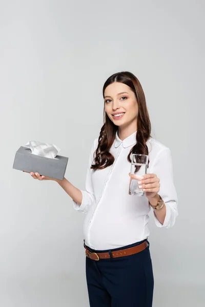 Lächelnde junge schwangere Geschäftsfrau mit Servietten und Wasser isoliert auf grau — Stockfoto