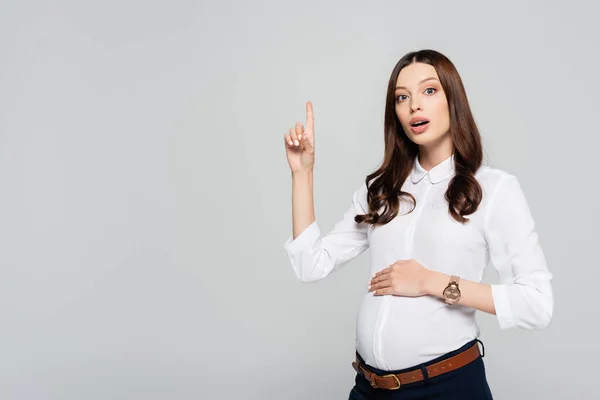 Schockierte junge schwangere Geschäftsfrau zeigt mit erhobenem Zeigefinger isoliert auf grau — Stockfoto