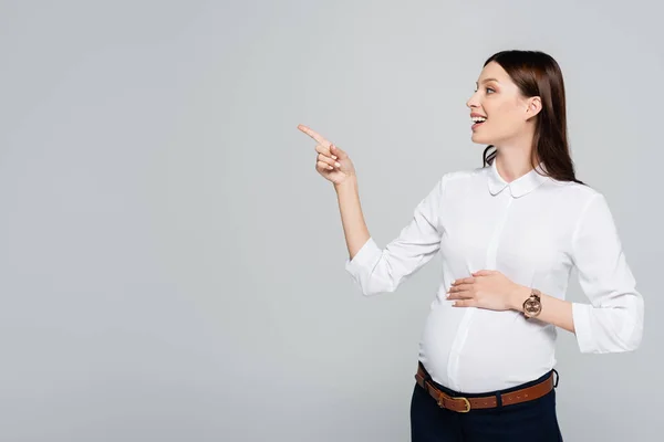 Souriant jeune femme d'affaires enceinte pointant de côté isolé sur gris — Photo de stock